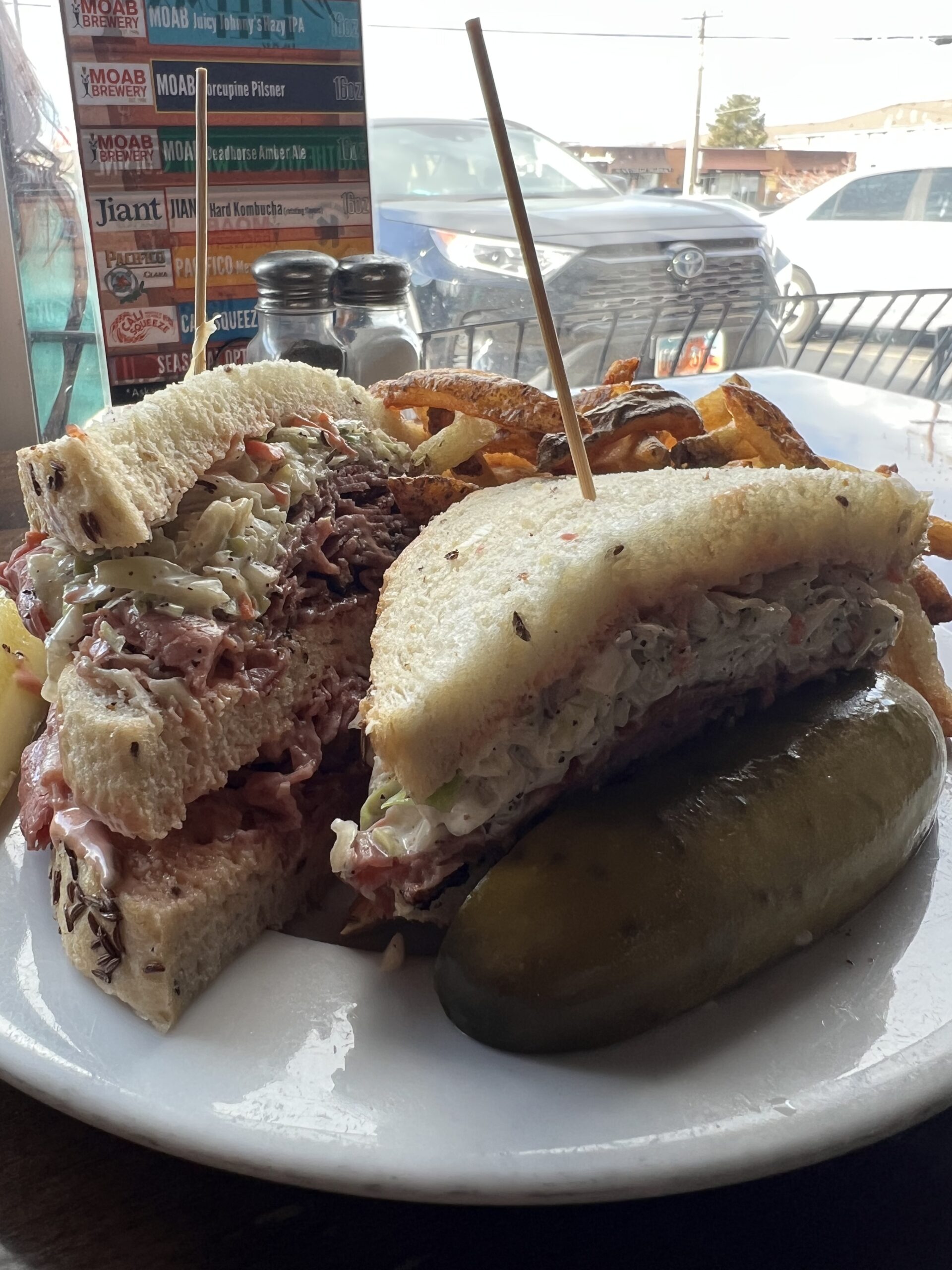 A mouth-watering Sloppy Joe from Feldman's Deli, piled high with pastrami and corned beef on Jewish Deli Rye, accompanied by crisp coleslaw, a juicy pickle, and golden, crispy fries.